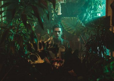 Chris Emray - Aufnahme aus Musikvideo Sleepwalking - Chris steht vor Garage und schaut durch Dschungelpflanzen im Wohnzimmer