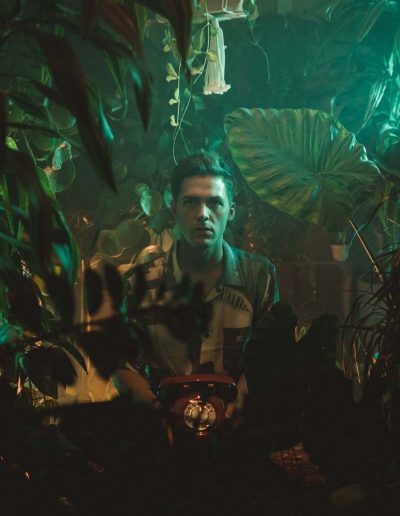 Chris Emray - Aufnahme aus Musikvideo Sleepwalking - Chris steht vor Garage und schaut durch Dschungelpflanzen im Wohnzimmer
